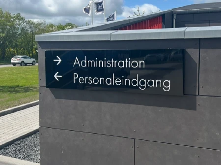 Grå totem-pylon med retningspile til administration og personaleindgang