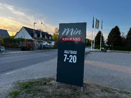 Fritstående skilt med logo og åbningstider ved indkørsel